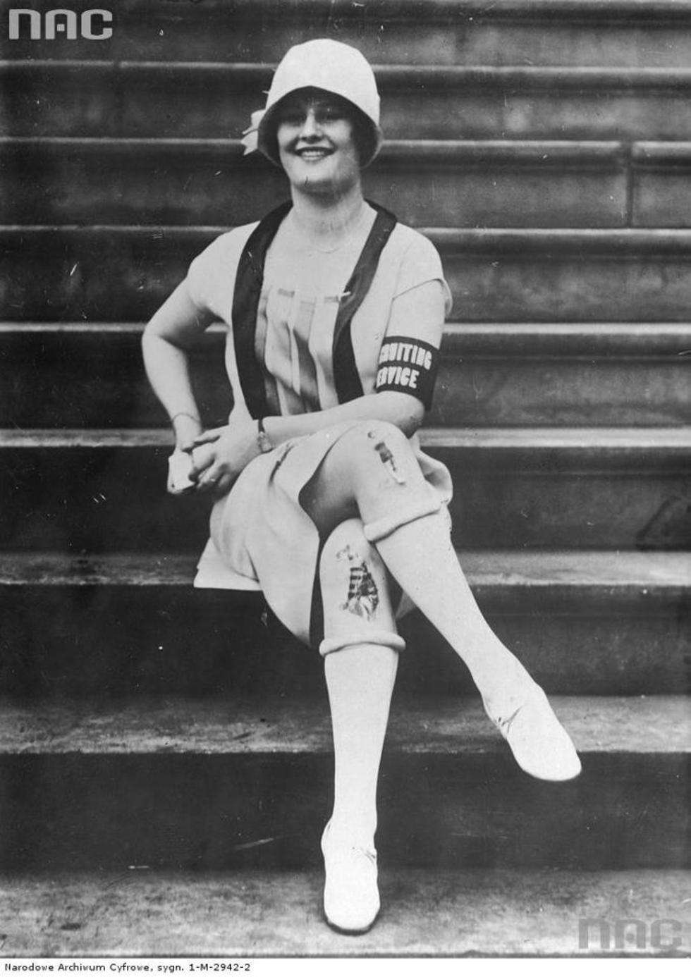  Kobieta w sportowym stroju, podkolanówkach, kapelusiku i ozdobami na kolanach.