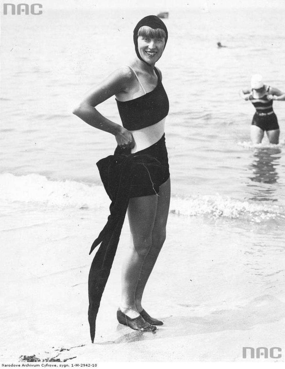  Kobieta na plaży w welwetowym kostiumie kąpielowym z kokardą u boku i czepku.