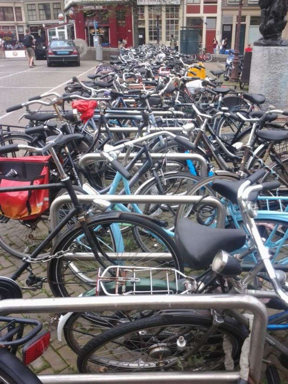  Zdjęcie zostało zrobione podczas przejażdżek do
Amsterdamu. Startowałem z miejscowości Aalsmeer, gdzie pracowałem i mieszkałem, przejeżdżałem przez Park Amsterdamski (Amsterdamse Bos) i znajdowałem się w południowej dzielnicy stolicy Holandii obrośniętej przez biznesowe wieżowce. Z tamtych rejonów niezbyt interesujących i zbyt oczywistych, jechałem zazwyczaj do centrum miasta. Szereg zaparkowanych rowerów pokazany na zdjęciu znajduję się niedaleko dzielnicy Czerwonych Latarnii i cofeeshopu The Jocker 