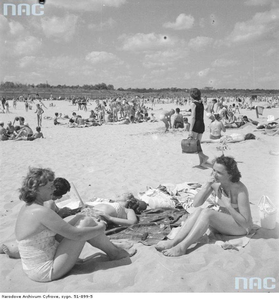  Rok 1958. Letnicy w strojach plażowych opalający się nad morzem. Na pierwszym planie siedzą rozmawiające ze sobą dwie kobiety.