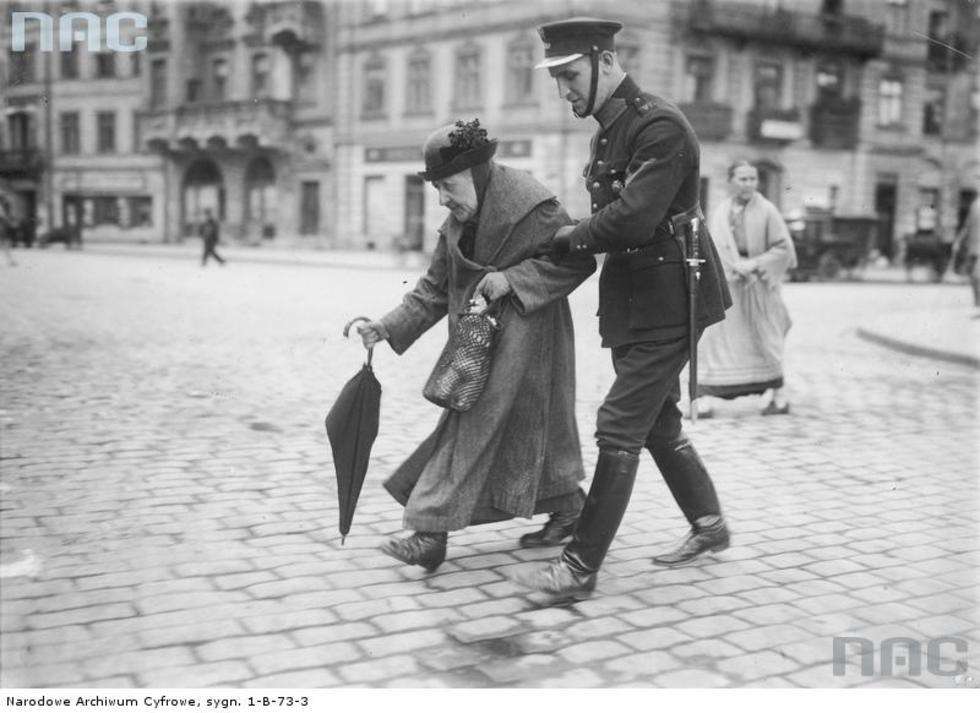  Zdjęcie z lipca 1925 roku. Policjant przeprowadza staruszkę przez ulicę w Warszawie. 