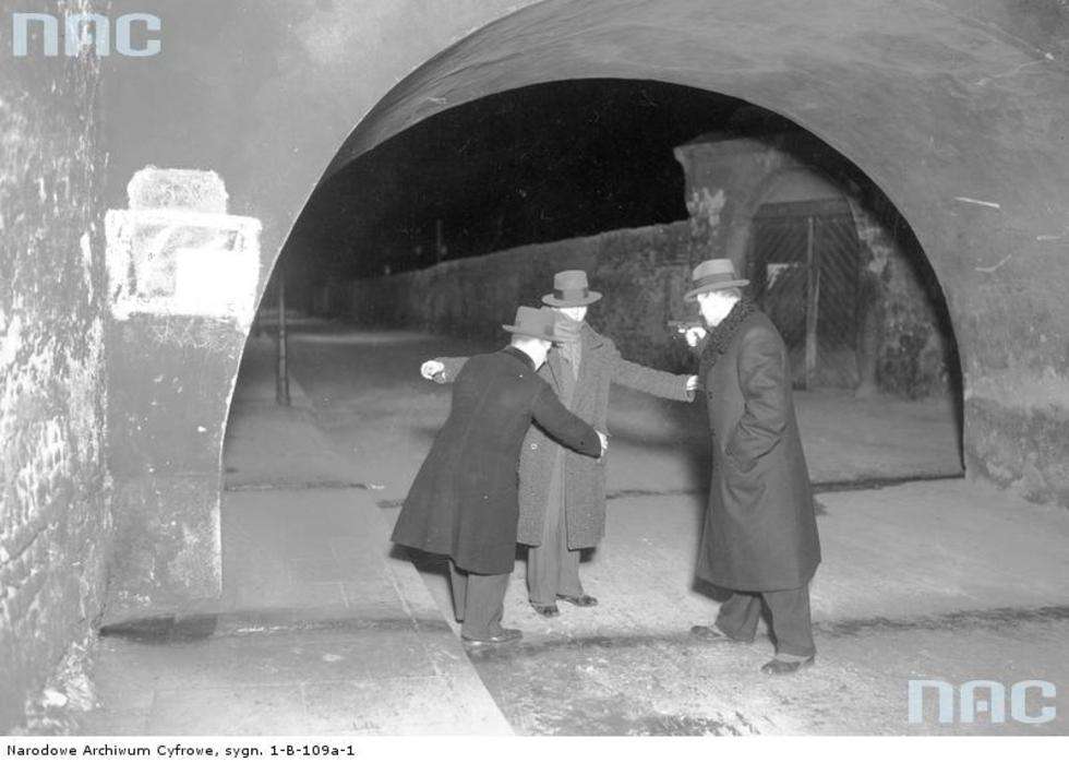  Zdjęcie z lat 30. Policjanci przeszukują zatrzymanego mężczyznę. 