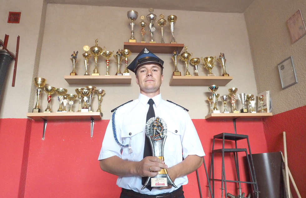  <p>Kamil Paśnik, naczelnik OSP Juliopol ze statuetką dla najlepszej jednostki. W tle kolekcja strażackich nagr&oacute;d</p>