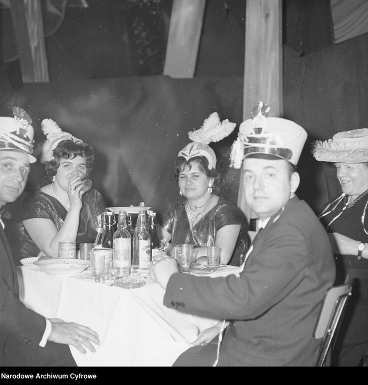  <p>Goście w przebraniach siedzą przy stoliku lata 60-te</p>