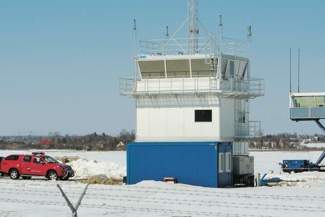 Istniejąca wieża ma trzy kondygnacje i zbudowana jest z sześciu kontenerów. Z prawej – mobilna wieża, której używano w pierwszej fazie funkcjonowania lotniska