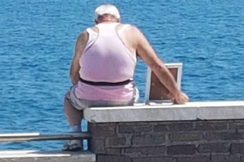 Mężczyzna ma na imię Giuseppe i regularnie siedzi na kamiennym murku nad morzem z fotografią w ramce