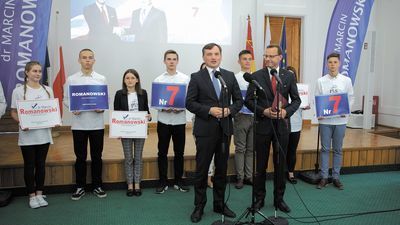 Podczas konferencji za ministrami stali młodzi ludzie ubrani w koszulki z logo PiS i nazwiskiem Romanowskiego, trzymający plansze z cyfrą 7