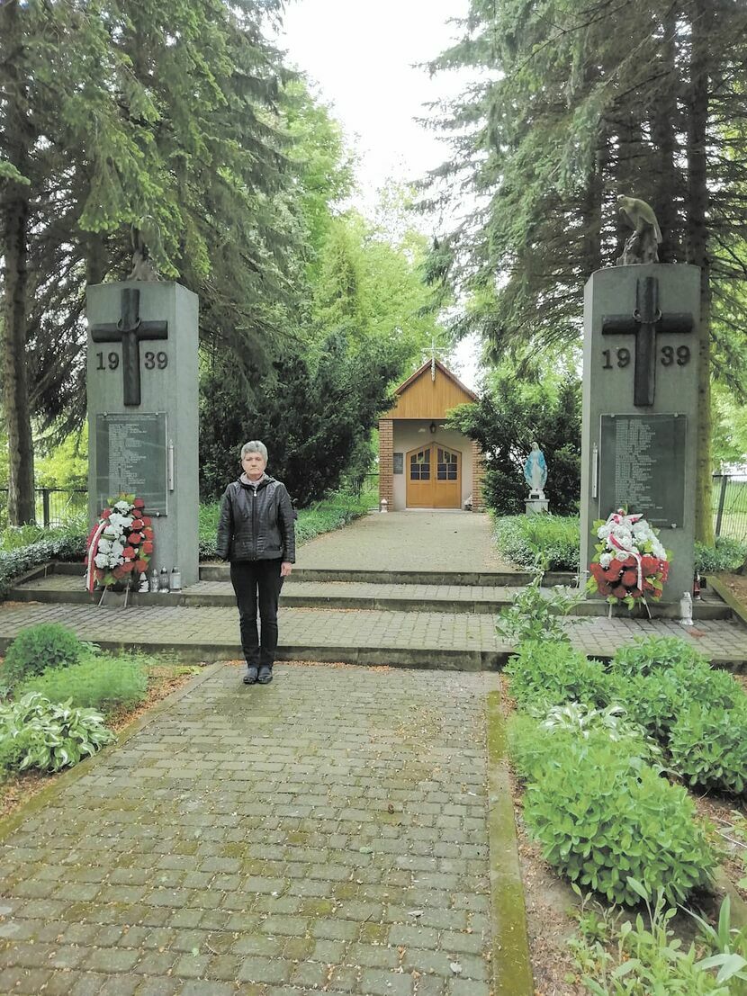 Bogusława Anna Grzelak przed pomnikiem i kapliczką upamiętniającą hitlerowską zbrodnię 