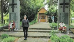 Bogusława Anna Grzelak przed pomnikiem i kapliczką upamiętniającą hitlerowską zbrodnię 