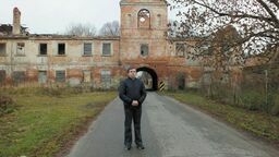 Tomasz Stańczuk na tle zrujnowanej oficyny Zarządu Dóbr Włodawskich Zamoyskich w Różance