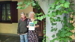 Agnieszka Drwal i Maria Skowrońska-Drwalowa z dyplomem Skarbu Kultury Przestrzeni przy winorośli pod arkadą budynku na Wyszyńskiego 4